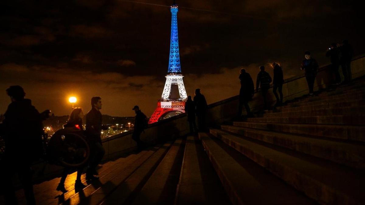 People walk and take pictures in front of the Eiffel Tower illuminated in the French colors in honor of the victims of the attacks last week in Paris.
