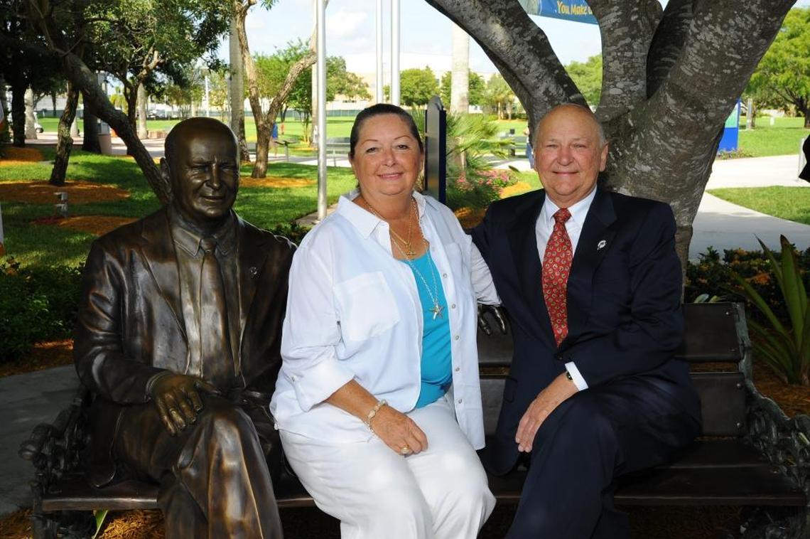 The late Marti and Wayne Huizenga sit on a park bench on the Nova Southeastern University campus next to a statue of Wayne Huizenga in 2013.