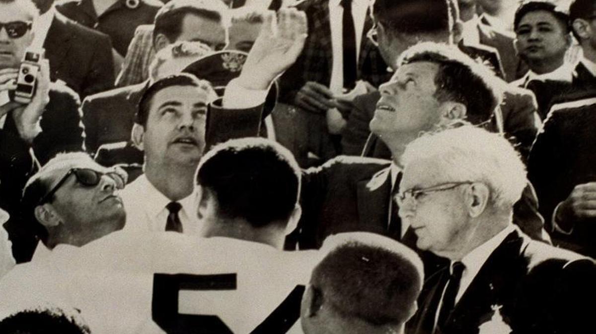 In this photo from January 1963, President John F. Kennedy tosses a coin from the stands prior to the start of the Orange Bowl football game between the University of Alabama and the University of Oklahoma. JFK Library