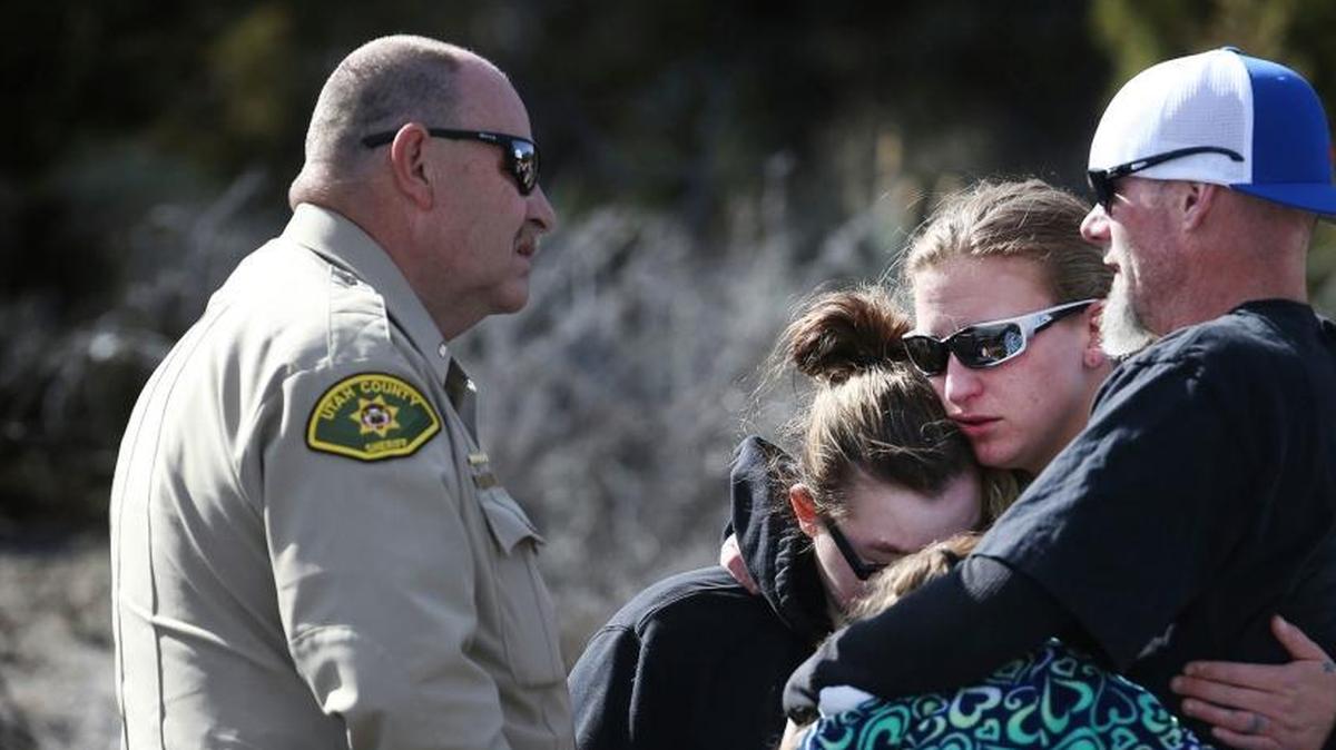 A police officer watches as Kylysta Otteson, Brelynne "Breezy" Otteson's sister, Emalee Otteson, Brelynne's stepmother, Kenny Otteson, Brelynne's father, and Anisty Shoemaker, Brelynne's sister, console one another after two bodies were recovered 100 feet down an abandoned mine shaft outside Eureka, Utah.