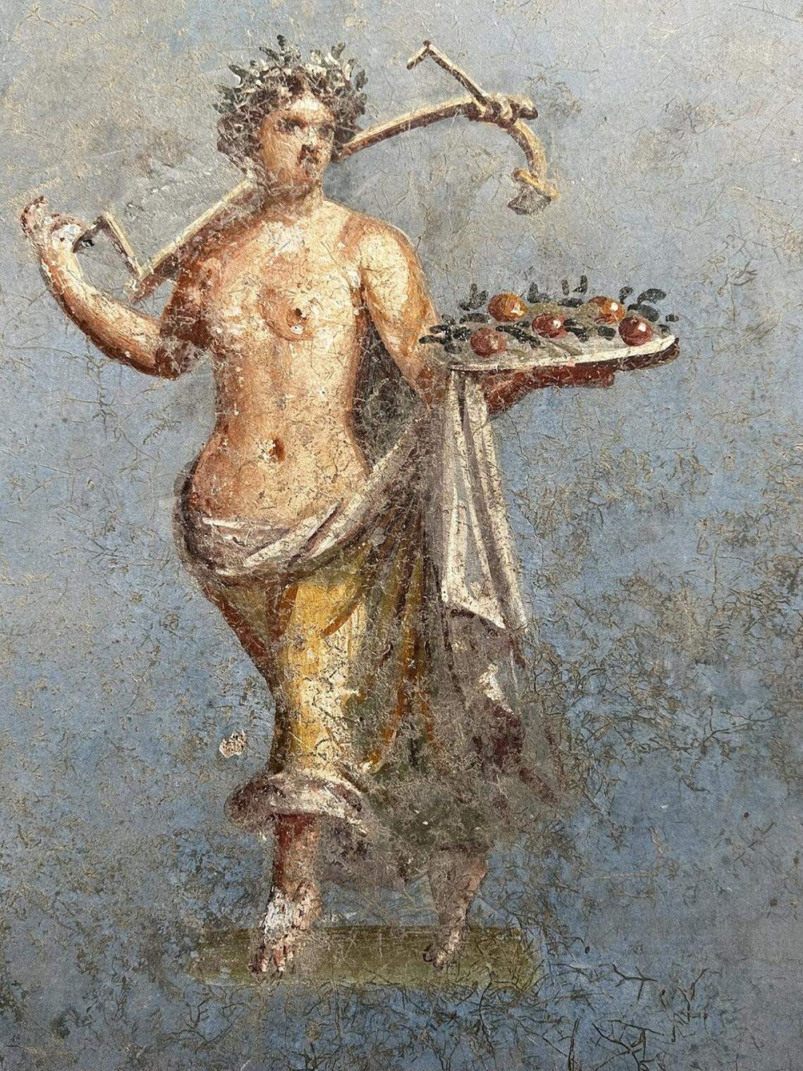Painting of a female figure holding a platter of fruit in one hand and an agricultural tool in the other