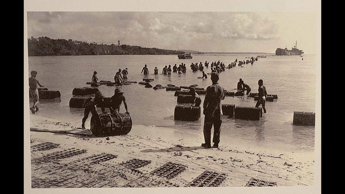 U.S. soldiers unload supplies on a Pacific island beach during World War II with pierced steel planking (PSP) in the sand in the foreground.