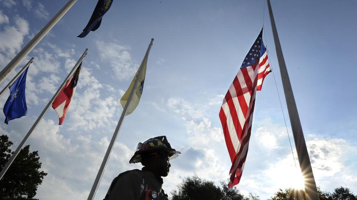 As the early morning sun begins to break above the trees, firefighter Alwyn Chandler, with the Fort Gordon Fire Department, stands beneath the flag following a 9/11 remembrance ceremony at Fort Gordon, Ga., Friday, Sept. 9, 2016.