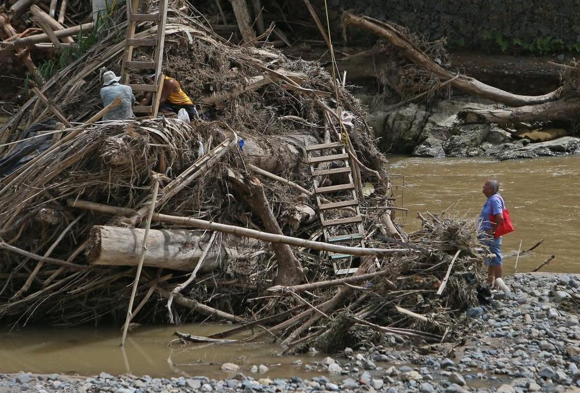 Rio Abajo residents Carlos Ocasio Borrero, left, and Luis Santiago cleaning debris as a resident waits to climb the ladder to the Rio Abajo neighborhood of Utuado, now known as the Camp of the Forgotten Ones, during the aftermath of Hurricane Maria in Puerto Rico.