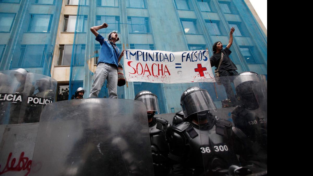 
In this April 7, 2011, file photo, students hold up a sign that reads in Spanish “Impunity Soacha equals false positives” during a protest where police stand guard in Bogota, Colombia. Military jargon identifies a “positive” as a slain enemy combatant. Authorities are investigating some 3,900 cases of alleged extrajudicial killings involving security force members. 
