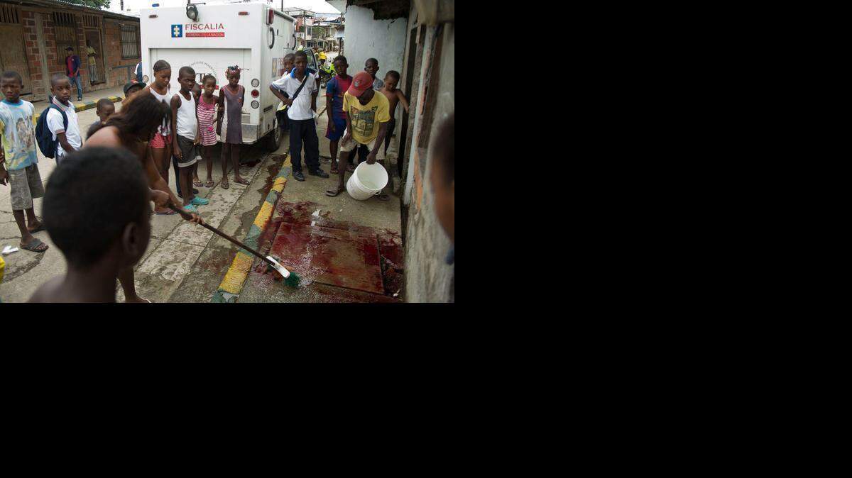 
A woman cleans up blood after officials have removed the body of a murder victim and placed it in a refrigerated truck (rear) for transport to the Medical Examiner's Office. 
