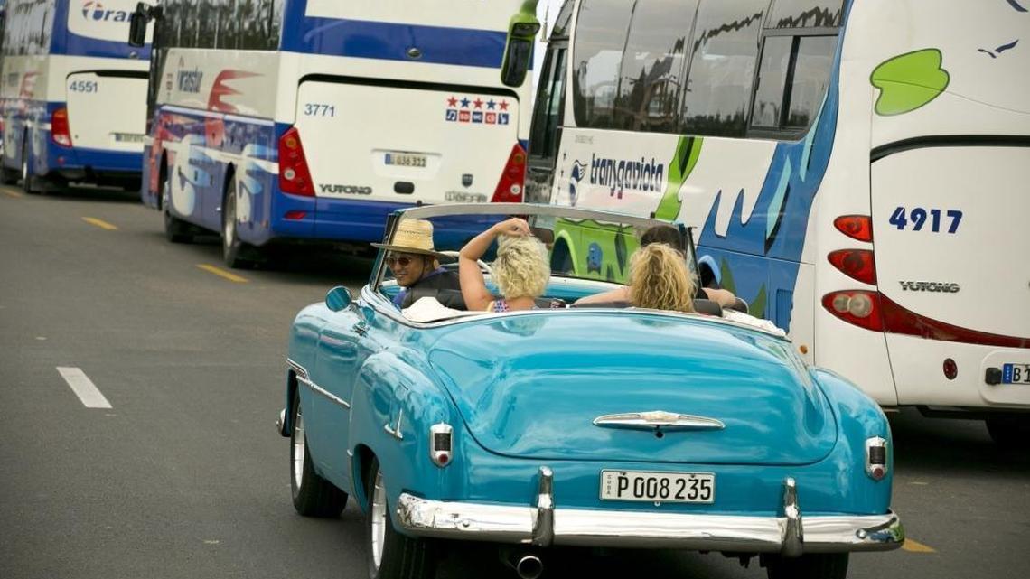 Visitors to Cuba ride a vintage convertible while touring Old Havana with tour buseslined up along the Malecon in the background. Individuals now make their own people-to-people trips to Cuba.