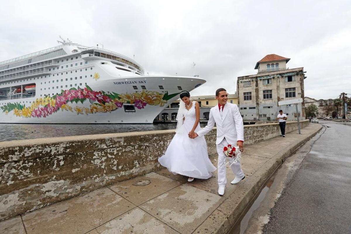 Newlyweds walk hand-in-hand down a wet and windy street following a photo shoot in front of the Norwegian Sky cruise ship.