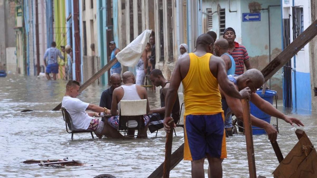 In this photo released by Granma, men play dominoes in the middle of a flooded street as others pull broken furniture from calf-high water in the aftermath of Hurricane Irma, in Havana.