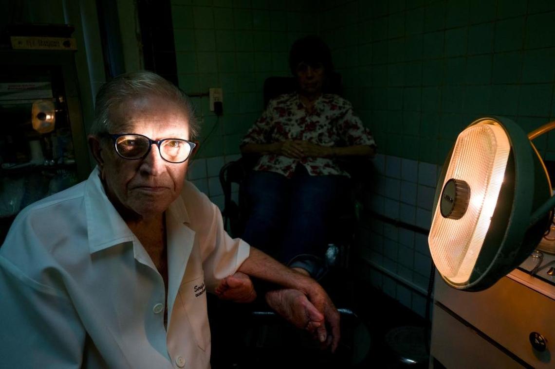 In this June. 8, 2017 photo, podiatrist Serafin Barca poses for a photo with a patient in his clinic in Havana, Cuba. The 80-year-old podiatrist is one of the last private medical workers in communist Cuba, which prides itself on its free, universal state health care.