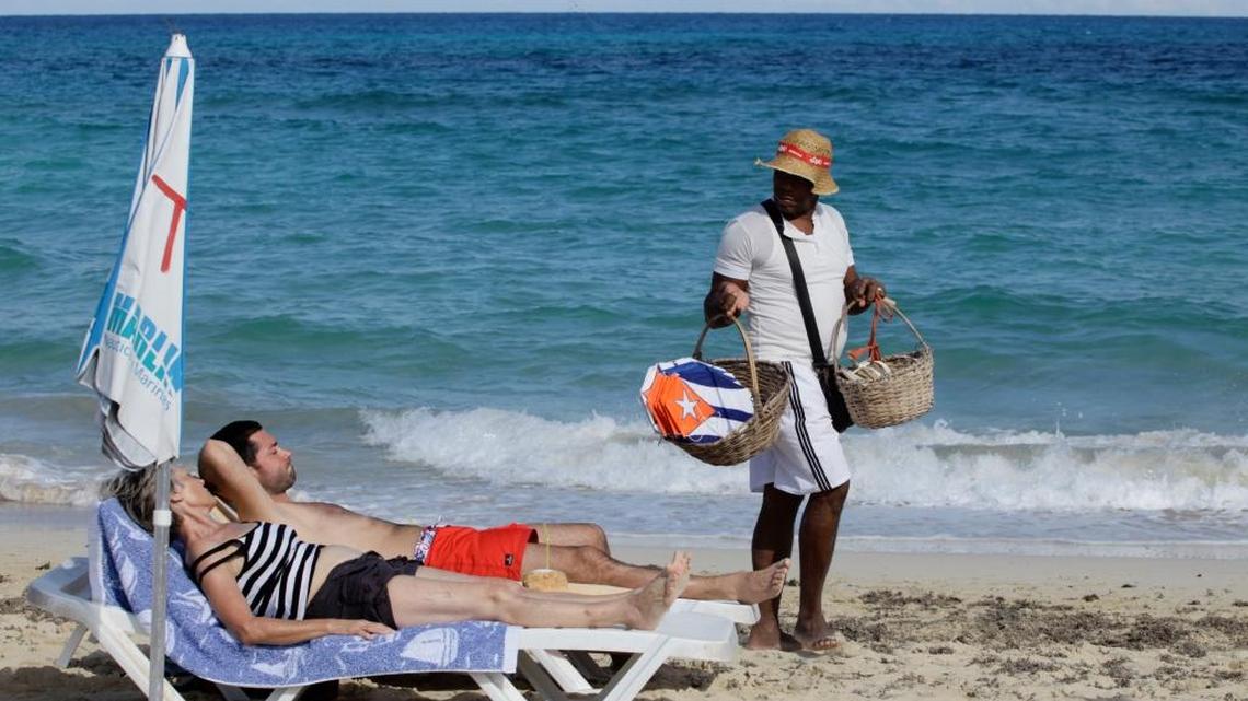 Tourists sunbathe as a vendor sells kites decorated with Cuba’s flag on a beach near Havana. Recent commentary in Cuba has taken on tourism inequality. Cubans complain that foreigners are often treated better than they are at the island’s tourism facilities.