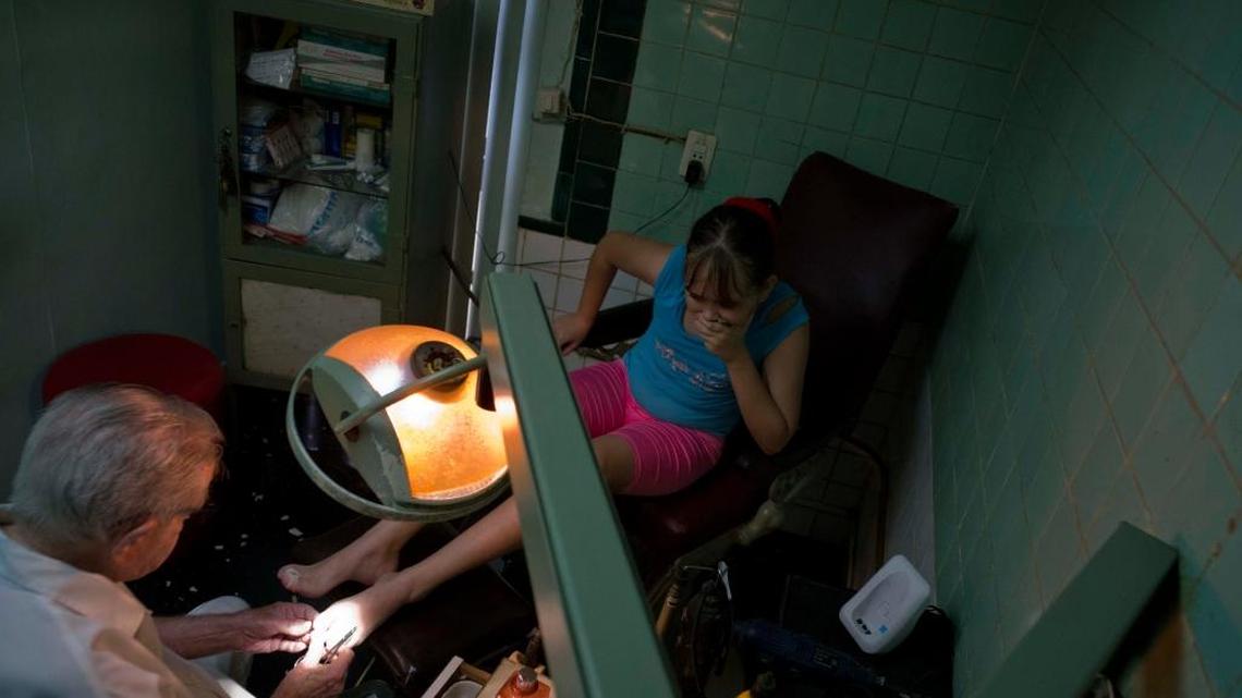 In this June. 8, 2017 photo, podiatrist Serafin Barca attends a patient in his clinic in Havana, Cuba. Barca is legally allowed to charge for his services because he graduated before Cuba's 1959 revolution.