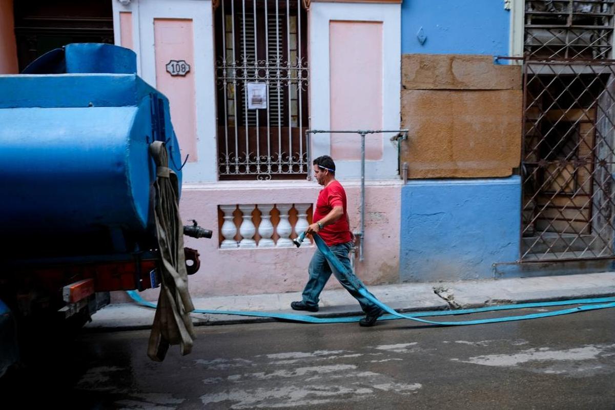 Outside on a street called Aguacate, Yan Alvarez pipes water into the home of Yanin Amaga, who waits for water to come every seven days. Amaga says if her neighborhood needs more water, residents have to call the water company. Only then will they come back.