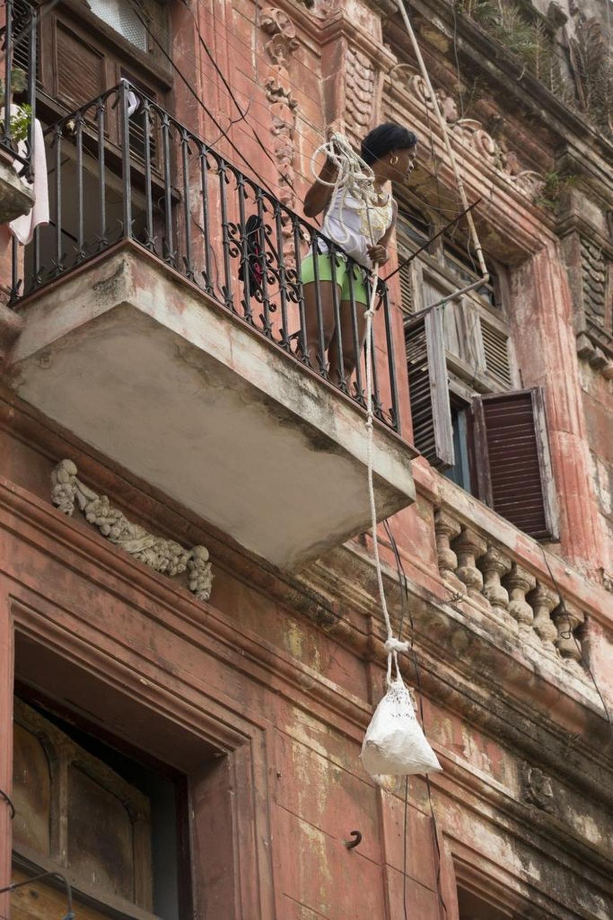 A Cuban woman uses a rope and bag to haul up her belongings to her Havana home, one of many decrepit buildings in the capital.