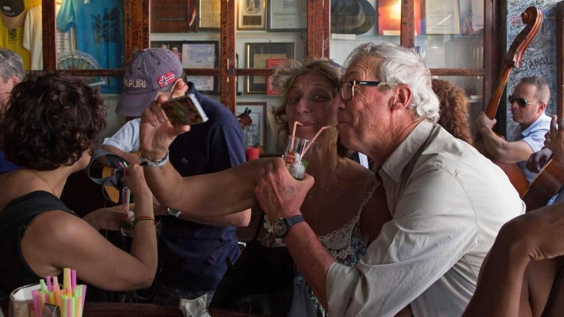 Tourists pose for a photo while sipping cocktail at the Bodeguita del Medio Bar in Old Havana. Although certain brands of Cuban rum and soft drinks are on a U.S. prohibited list, Treasury has clarified that American travelers can still purchase them while in Cuba as long as they don’t buy directly from the manufacturers.