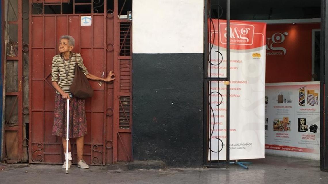 An elderly woman stands outside an apartment building in Havana.