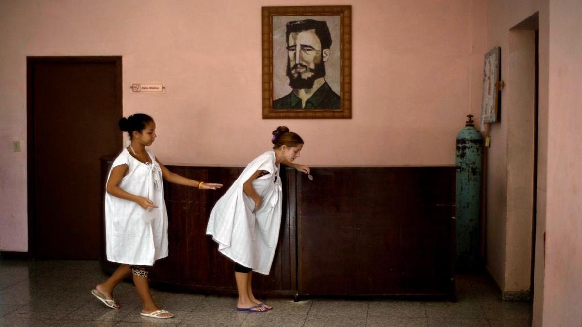 In this Oct. 27, 2014 photo, a pregnant woman is helped by another as she suffers from labor pains, while walking in front of a painting of Fidel Castro at a special maternity unit for high-risk pregnancies in Havana, Cuba.