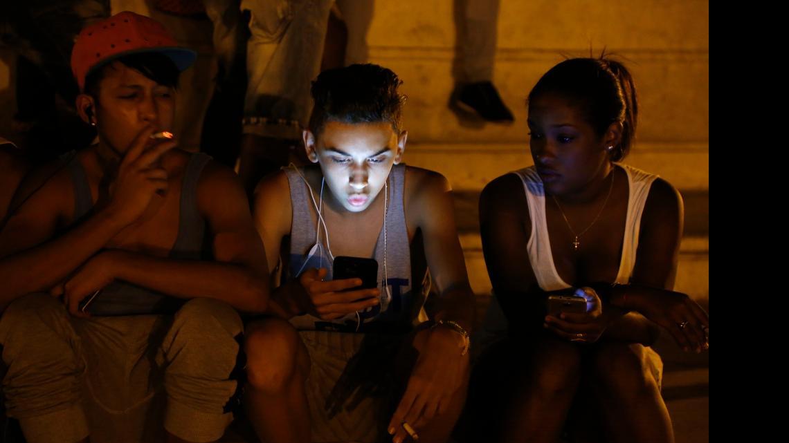 
To be young and connected: Cuba young people use a password protected Wi-FI network from a nearby five-star hotel to surf the Internet on their Smartphones in downtown Havana. Cubans are hungry for better Internet connections.
