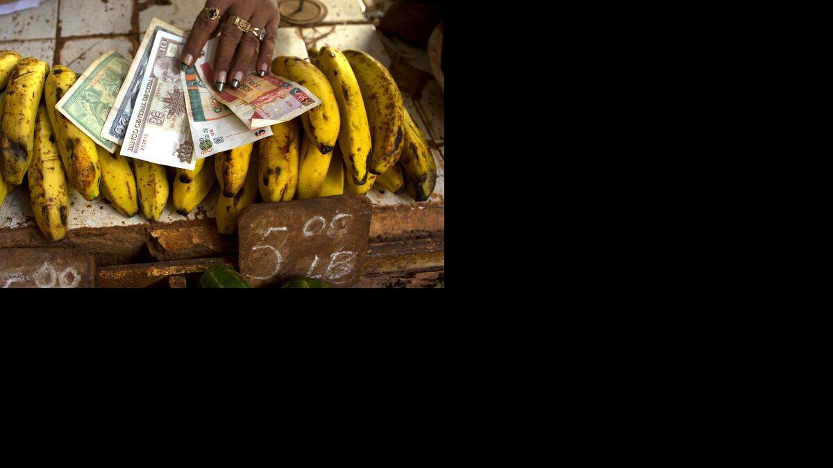 
In this Aug. 30, 2013 file photo, a food vendor spreads out convertible pesos, known as CUCs, the two bills on the right, and regular Cuban pesos at her stand in a vegetable market in Havana, Cuba. Cuba’s central bank says elimination of the special currency, CUCs, will require putting more Cuban pesos into circulation and issuing higher-denomination bills. Most Cubans earn and buy goods in local pesos, and the convertible peso (CUCs) are used largely in the tourism sector. 
