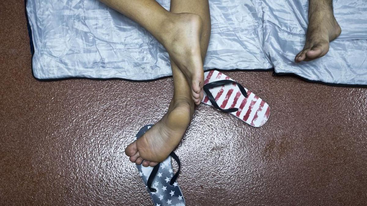 In this Nov. 21, 2015 file photo, flip flops decorated with a U.S. flag motif lay next to its owner, a Cuban migrant sleeping inside of the public restroom inside the border control building in Penas Blancas, Costa Rica, on the border with Nicaragua. Once Cubans reach the U.S. border, they can just show up at an established U.S. port of entry and declare their nationality, avoiding the dangerous desert crossings that confront many migrants who try to avoid U.S. border patrol.