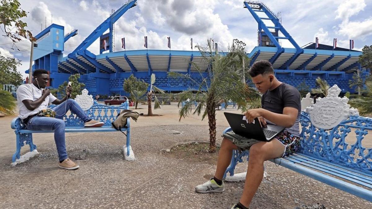 The Tostonet venture repairs laptops, PCs and other devices. Although the nine employees can compete together for contracts, they all hold their own licenses as self-employed workers. Here Manuel Mendez, left, and Pedro Jordan, right, take advantage of the free WiFi outside the Estadio Latina Americano in Havana.