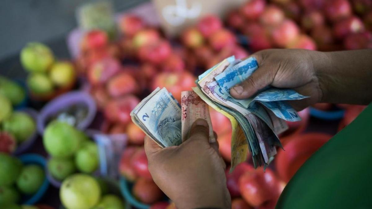 In this Sept. 24 ,2015 photo, a fruit vendor counts his Real bills at a street market in Rio de Janeiro, Brazil.