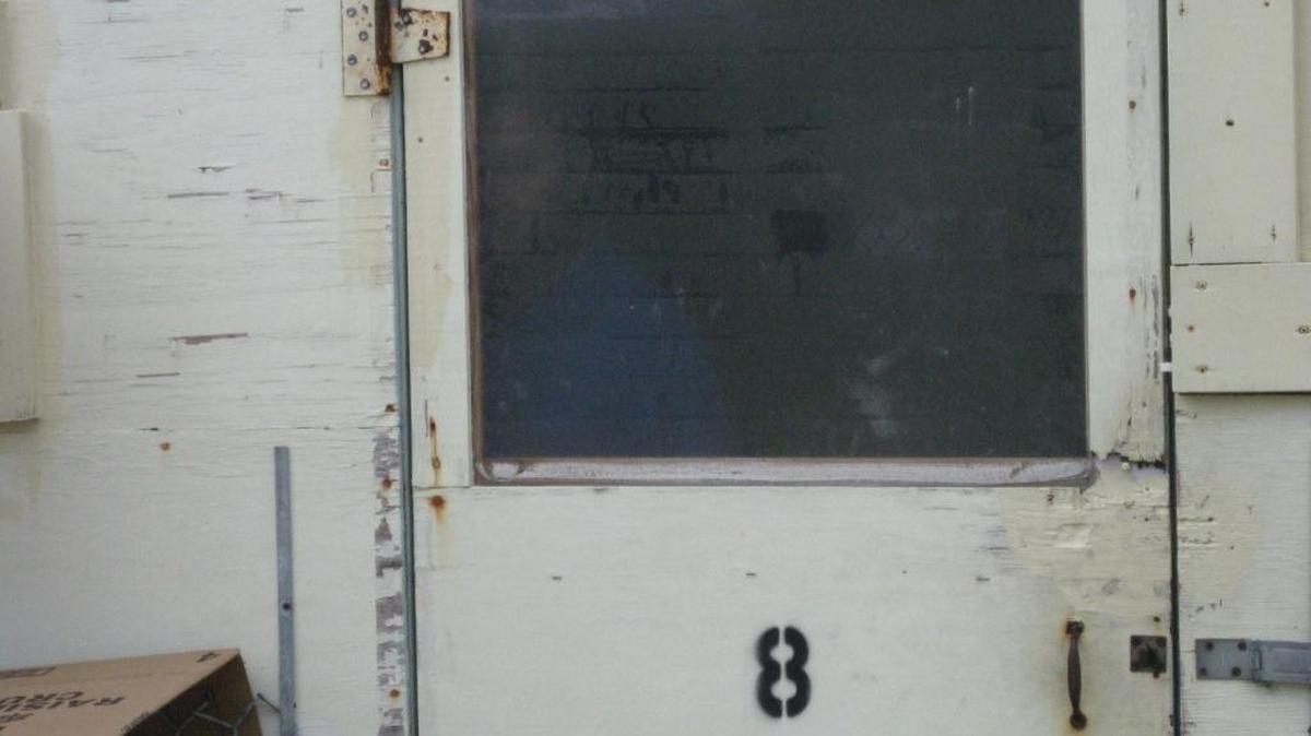 In shadows, a Uighur Muslim detainee hides inside a plywood hut at Camp Iguana on Monday, June 1, 2009, moments after a spontaneous poster-board protest in this image approved for release by the military at the U.S. Navy base at Guantánamo Bay, Cuba.