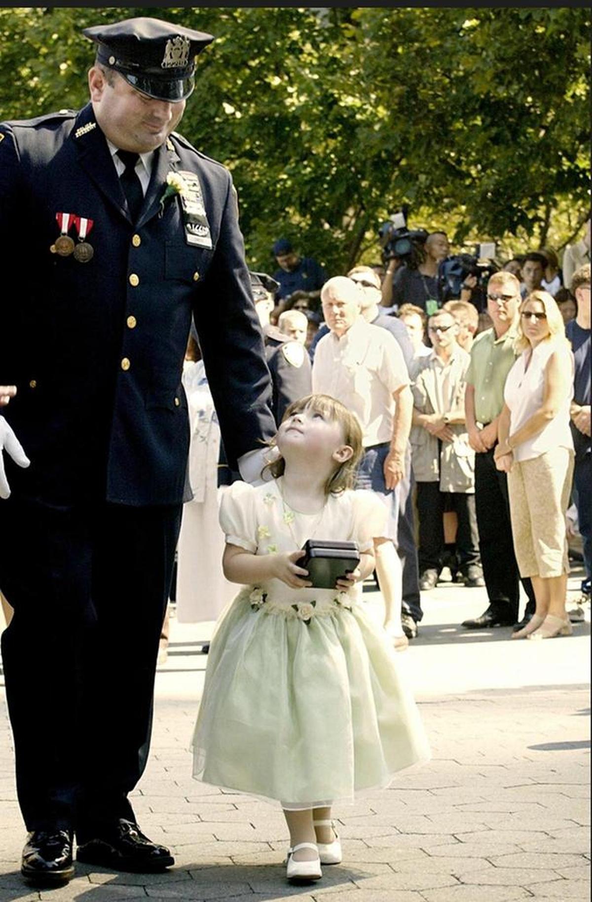 New York Police officer James Smith escorts his 2-year-old daughter Patricia as she carries her mother’s police badge during a ceremony for the unveiling of 25 new names added to the Police Memorial at Battery Park, Mon., Sept. 9, 2002 in New York. Smith lost his wife NYPD Officer Moira Smith in the 9/11 attack on the World Trade Center.