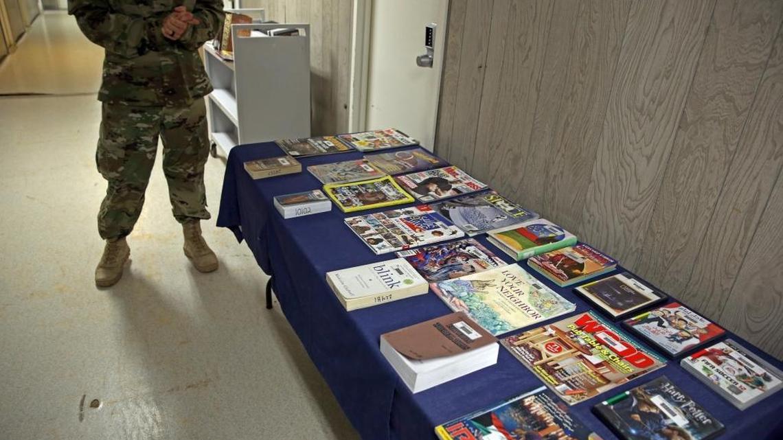 The officer in charge of detainee programs, including the detainee library, stands with displayed detention center books and videos during a media tour at the U.S. Navy base at Guantánamo Bay, Cuba, on Tuesday, Feb. 9, 2016, in this photo approved for release by the U.S. military. The military would not allow the officer’s face to be shown.