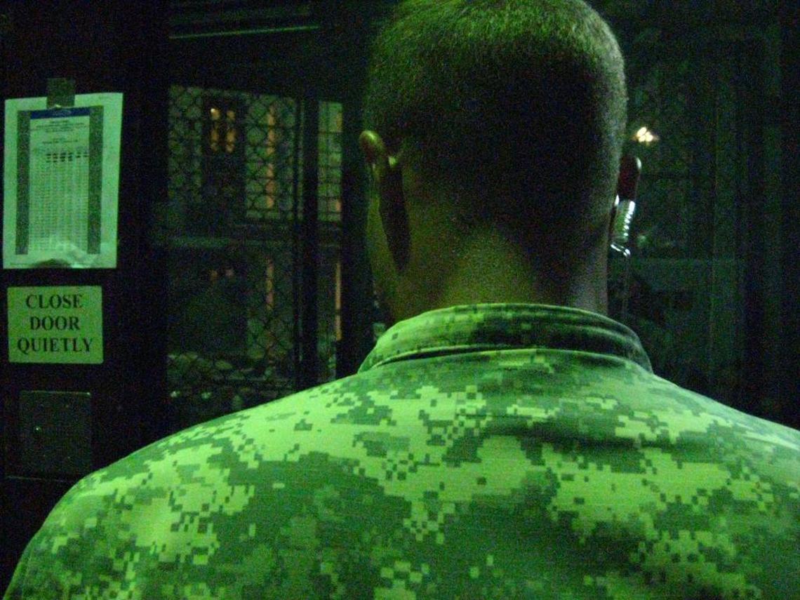 An Army guard stands watch outside a cellblock at the communal Camp 6 prison at the Guantánamo Detention Center on Saturday, June 3, 2017, in an image approved for release by the U.S. military. To his left, pasted on the wall: A Ramadan prayer schedule.