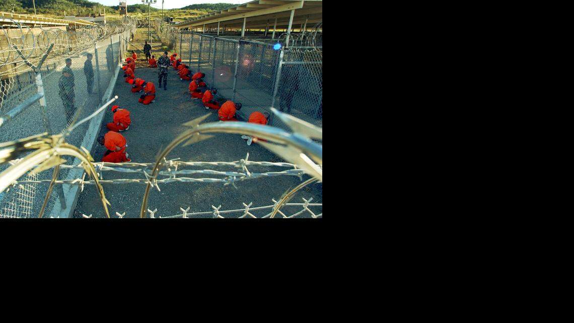 
In this handout photo from the Department of Defense, Taliban and al-Qaida detainees in orange jumpsuits kneel in a holding area at Camp X-Ray at Navy Base Guantánamo Bay, Cuba, under watch by Army MPs the day the detention center opened, Jan. 11, 2002. 
