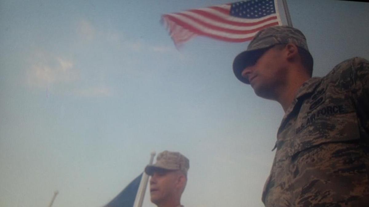Tech Sgt. Michael Badilla, a paralegal on the Sept. 11 trial, reenlists on Oct. 26, 2015 in a ceremony at the Camp Justice sign at the war court compound at the U.S. Navy base at Guantánamo Bay, Cuba, in this image taken from a video of the event. At left, Marine Brig. Gen. John Baker, who administered the oath.