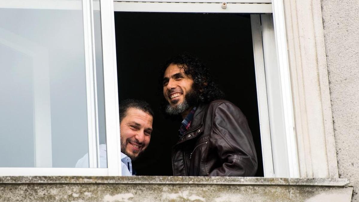 In this June 5, 2015 photo, Abu Wa'el Dhiab, from Syria, right, and Adel bin Muhammad El Ouerghi, of Tunisia, both freed Guantanamo Bay detainees, stand next to the window of their shared home in Montevideo, Uruguay.