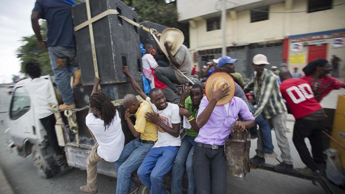 Protesters hitch a ride on an electricity generator being pulled by a sound truck, after police fire teargas during a protest against the country's electoral council in Port-au-Prince, Haiti, Saturday Dec. 12, 2015.