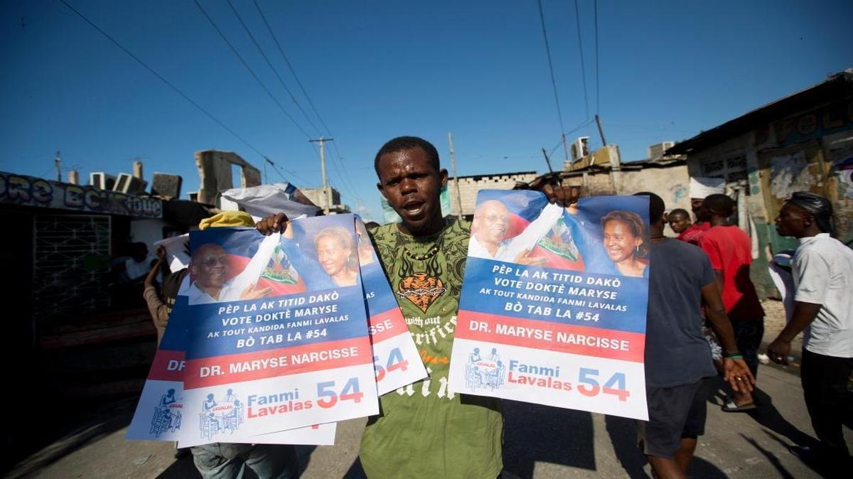 A supporter of presidential candidate Maryse Narcisse, from Fanmi Lavalas political party, holds campaign posters of former President Jean-Bertrand Aristide during a protest against election results in Port-au-Prince, Haiti, Tuesday.