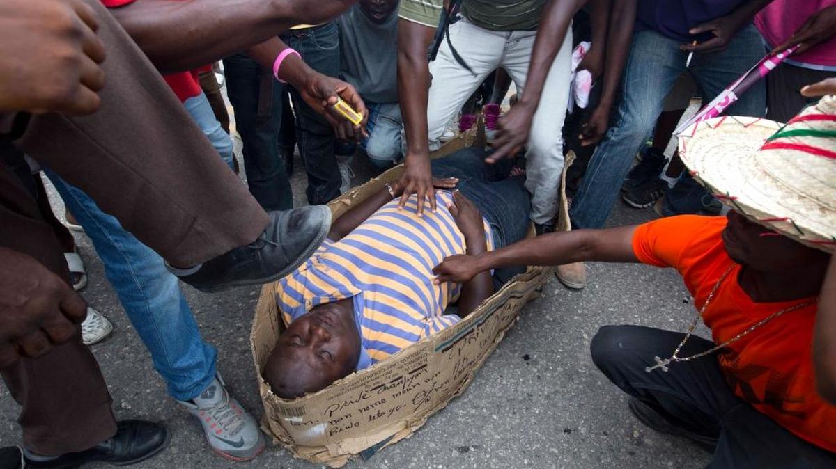 A supporter of the PHTK presidential candidate Jovenel Moise plays the role of provisional President Jocelerme Privert lying in a makeshift casket during a protest to demand the government restart the electoral process for a presidential runoff that has been postponed three times, in Port-au-Prince, Haiti, Thursday, April 28, 2016. The U.S. State Department's special coordinator for Haiti arrived Thursday seeking to help resolve a political standoff that has left elections in the Caribbean nation in limbo.