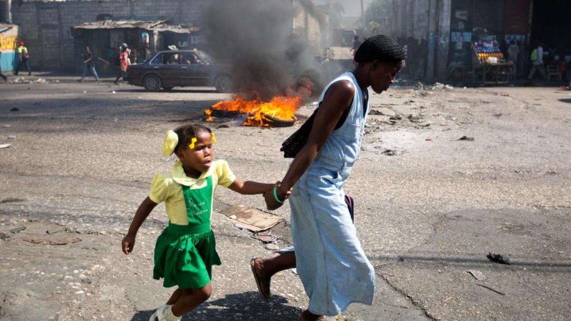 A woman and a child walk Monday past a burning barricade during a protest against President Michel Martelly's government to demand the cancellation of the Jan. 24 elections.