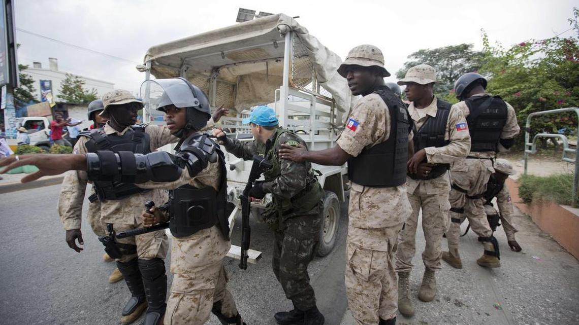 A UN Peacekeeper takes cover behind national police officers while demonstrators throw rocks, during a protest against the country's electoral council to mark the 25th anniversary of first democratic election in 1990, in Port-au-Prince, Haiti, Wednesday, Dec. 16. The demonstrators started throwing rocks after UN Peacekeepers from Brazil fired teargas into the crowd. Disputed election results have brought a renewed surge of paralyzing street protests and many broad accusations of electoral fraud from civil society and opposition groups that it is not clear whether a Dec. 27 presidential runoff between the top two finishers can take place as scheduled.