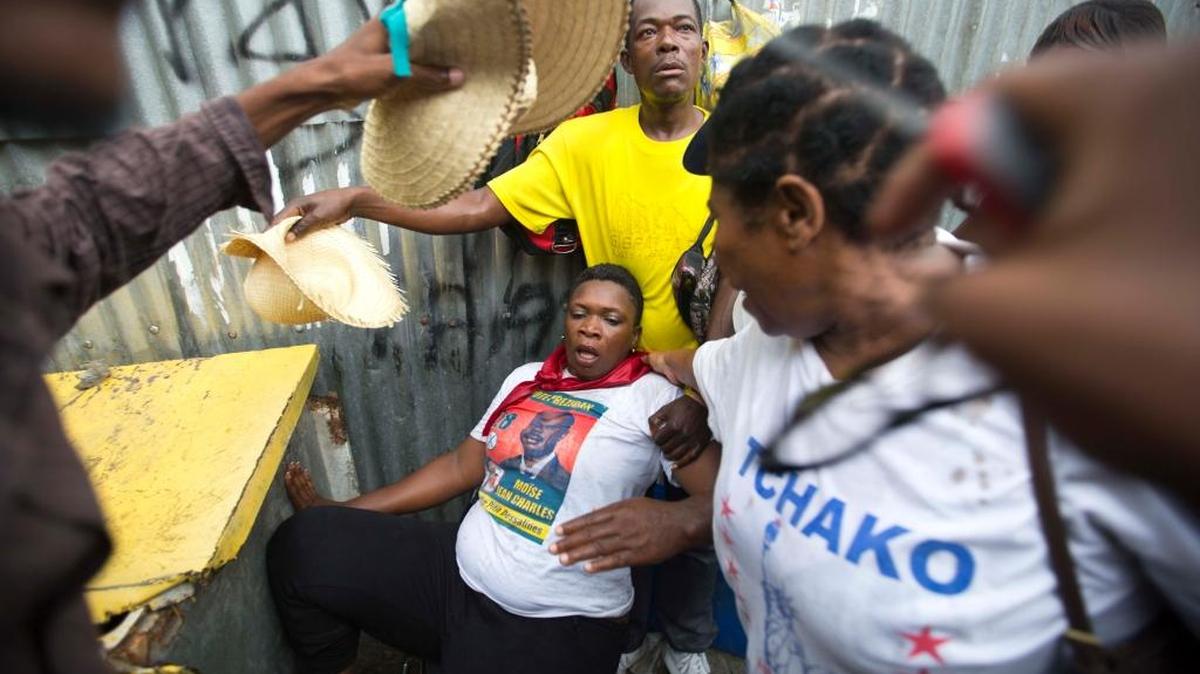 A woman is helped by fellow demonstrators after police fire teargas during a protest against the country's electoral council in Port-au-Prince, Haiti, Saturday Dec. 12, 2015. Disputed election results have brought a renewed surge of paralyzing street protests and many broad accusations of electoral fraud from civil society and opposition groups that it is not clear whether a Dec. 27 presidential runoff between the top two finishers can take place as scheduled.