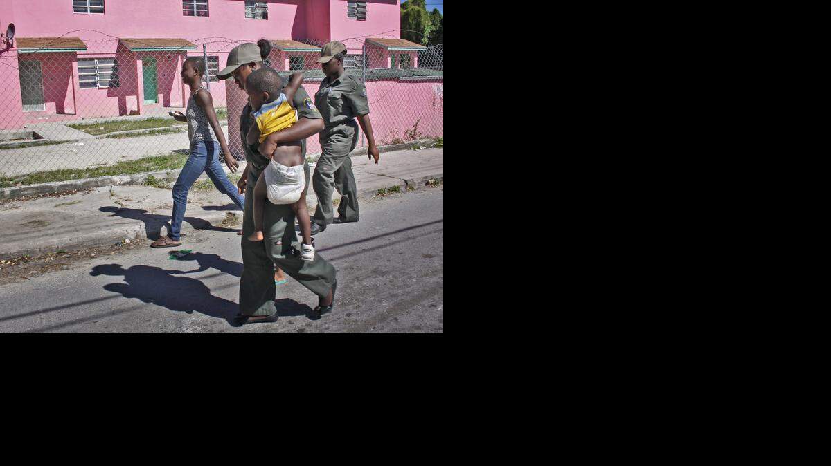 
Immigration officers escort a woman and child on to the immigration bus bound for the Carmichael Road Detention Center on Saturday, Novermber 1, 2014. Officials detained numerous suspected illegal immigrants during an island wide immigration raid.
