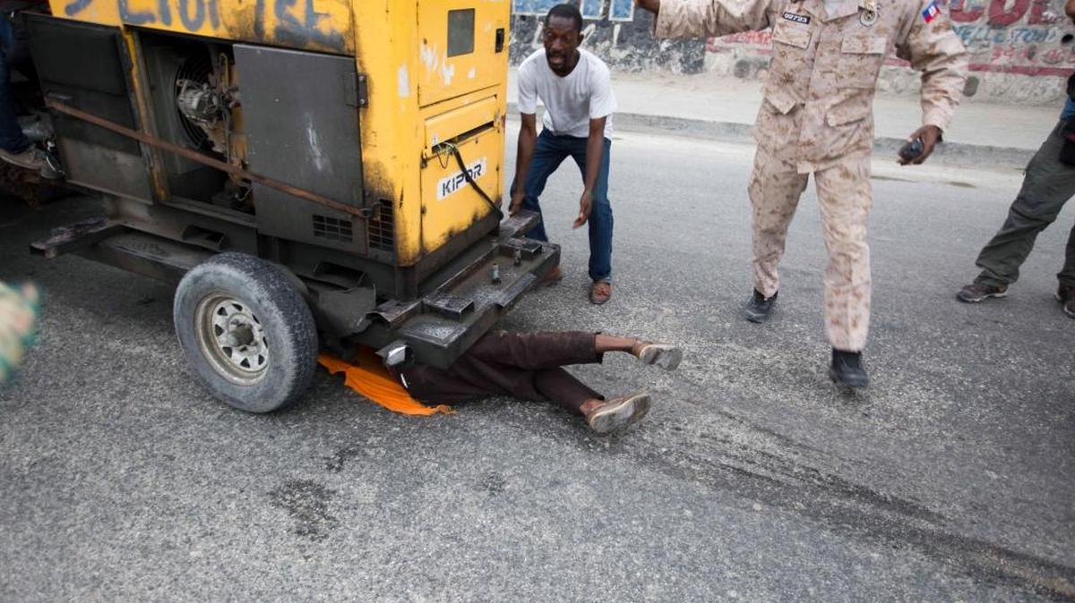 A demonstrator is dragged under a towed electricity generator after falling during clashes between police an protesters during a march against the country's electoral council in Port-au-Prince, Haiti, Saturday Dec. 12, 2015. He was rescued after other demonstrators lifted the generator and the police took him to the hospital where he was treated for his injuries.