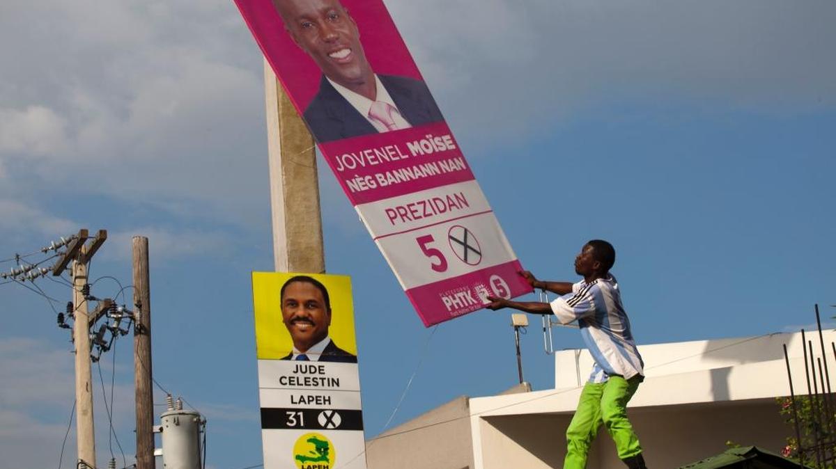 In this Nov. 12, 2015 file photo, supporters of presidential candidate Maryse Narcisse, of the Lavalas party, removes an election campaign sign of presidential candidate Jovenel Moise, in front of a sign of his rival, Jude Celestin, during a protest against election results in Port-au-Prince, Haiti. Celestin and the other presidential candidates that dub themselves the “Group of Eight” have been demanding an independent recount due to what they assert was “massive fraud” in favor of Moise, the government-backed contender in October elections.