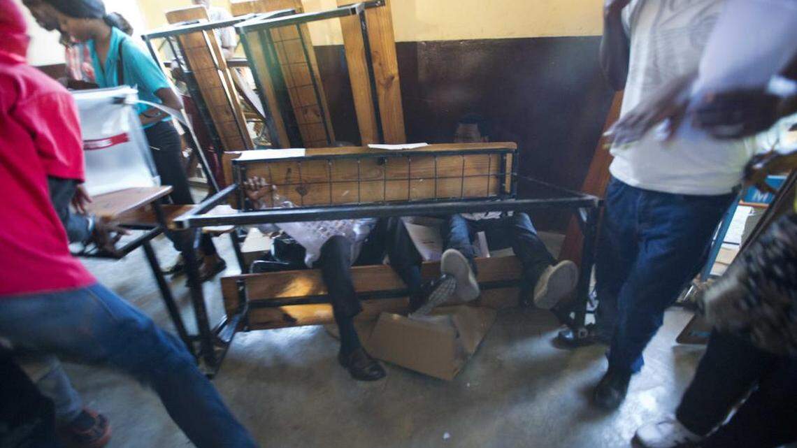 
People sitting on a desk are thrown to the ground after a fight broke out inside a voting center during parliamentary elections in Port-au-Prince, Haiti, Sunday, Aug. 9, 2015. Young men tore up paper ballots and rocks were thrown before police shut the center down.

