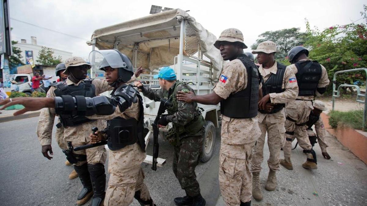 A UN Peacekeeper takes cover behind Haiti National Police officers while demonstrators throw rocks, during a protest against the country's electoral council to mark the 25th anniversary of first democratic election in 1990, in Port-au-Prince, Haiti.