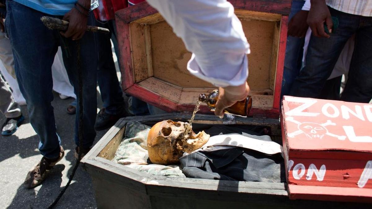 A supporter of the PHTK presidential candidate Jovenel Moise poors beer into a skull representing interim President Jocelerme Privert in a mock coffin, during a voodoo ceremony, before the start of a protest march demanding his resignation in Port-au-Prince, Haiti, Tuesday, June 7, 2016. The electoral council of Haiti has decided to re-do a presidential election that a special commission determined was marred by fraud.