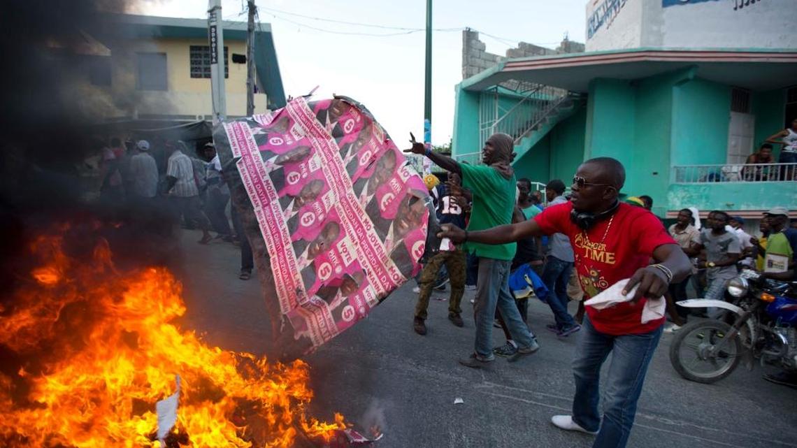 Protesters toss a campaign poster of government-backed presidential candidate Jovenel Moise onto a burning barricade during a protest against President Michel Martelly's government, in Port-au-Prince, Haiti, Saturday, Jan. 23, 2016. A presidential runoff that had already been delayed once and faced deep public skepticism was put on hold indefinitely Friday. The Saturday protesters are demanding that Martelly leave office Feb. 7, as is required under the Constitution, and an interim government take power.