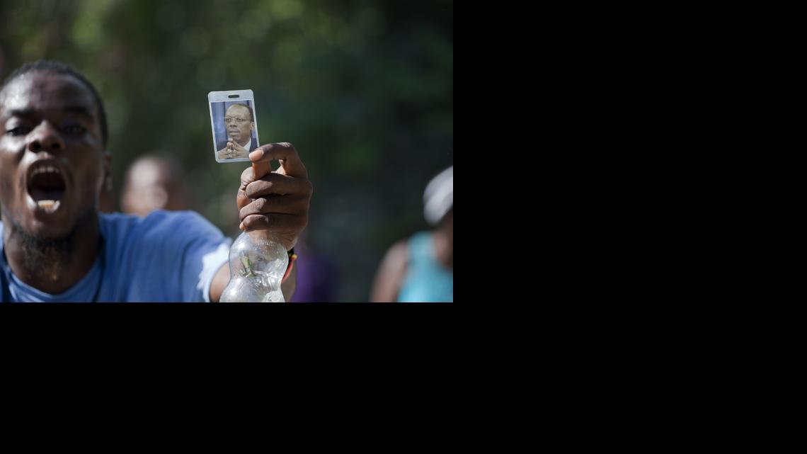 
A supporter of Haiti's former President Jean-Bertrand Aristide holds up a picture of him, while demonstrating in front of his house during a protest in his support, in Port-au-Prince, Haiti, Thursday, Aug. 21, 2014. Supporters of the former president have been blocking the street in front of his house as the popular former leader faces possible arrest for not providing court-ordered testimony in a criminal investigation. 
