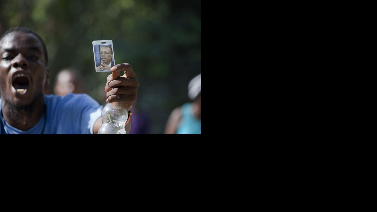 
A supporter of Haiti's former President Jean-Bertrand Aristide holds up a picture of him, while demonstrating in front of his house during a protest in his support, in Port-au-Prince, Haiti, Thursday, Aug. 21, 2014. Supporters of the former president have been blocking the street in front of his house as the popular former leader faces possible arrest for not providing court-ordered testimony in a criminal investigation. 
