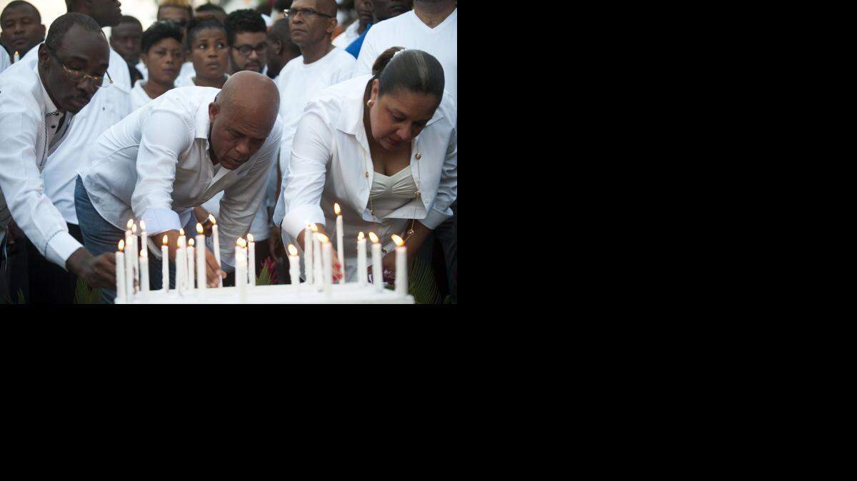 
Haitian President Michel Martelly, center, places a candle with First Lady Sophia Martelly, right, and Prime Minister of Haiti, Evans Paul, left, at the site of an accident during the march convened by the government in Port-au-Prince on February 17, 2015, in memory of the victims who died during celebrations in the National Carnival of Haiti. Haiti was plunged into mourning and Carnival festivities were cancelled after at least 16 people died when a high-voltage cable hit a parade float in the capital Port-au-Prince. 

