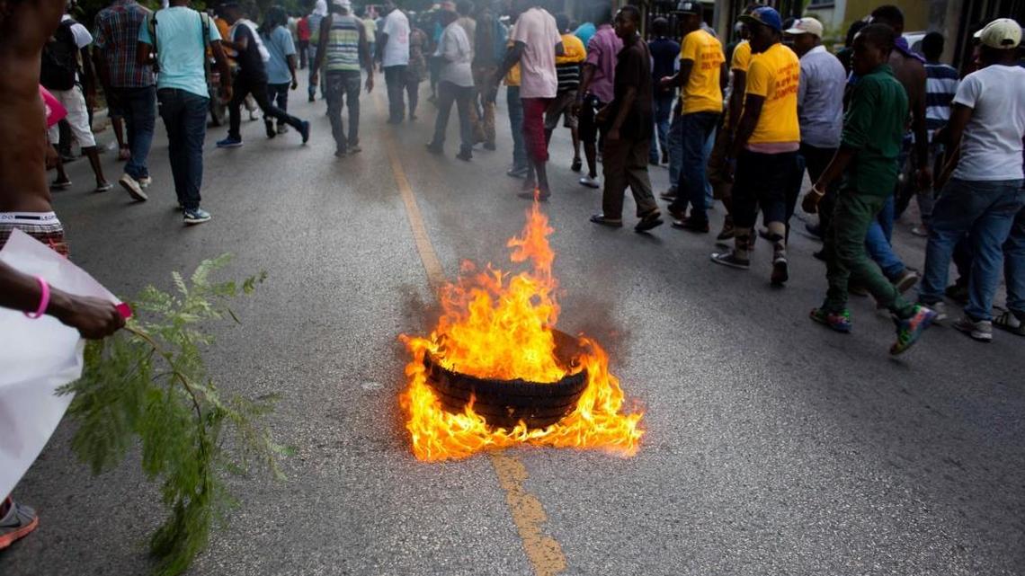 Supporters of the PHTK presidential candidate Jovenel Moise walk past burning tires during a protest march demanding the resignation of interim President Jocelerme Privert in Port-au-Prince, Haiti, Tuesday, June 7, 2016. The electoral council of Haiti has decided to re-do a presidential election that a special commission determined was marred by fraud.